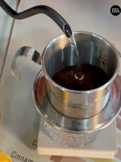 Pouring hot water into the Phin filter. The slow drip process is key to extracting the rich flavors of the Robusta coffee typically used.
