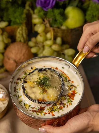 From our 'RUMI' Diwali menu, a baked cheese dish in a copper pot, garnished with dill and pistachios, embodying festive indulgence.