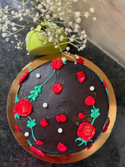 A rich Dutch truffle cake decorated with a beautiful pattern of hand-piped red roses and green leaves.