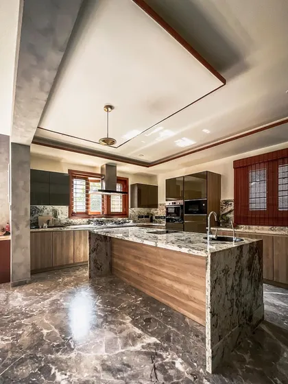 This statement kitchen combines functionality with luxury. It features a large island with a granite countertop, sleek handleless cabinetry, and premium built-in appliances, all set against a backdrop of elegant marble flooring.