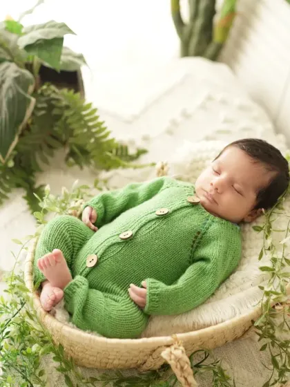 This newborn is dressed in a cozy green outfit, sleeping peacefully in a basket decorated with fresh greenery. We use natural elements to create an organic, earthy feel.
