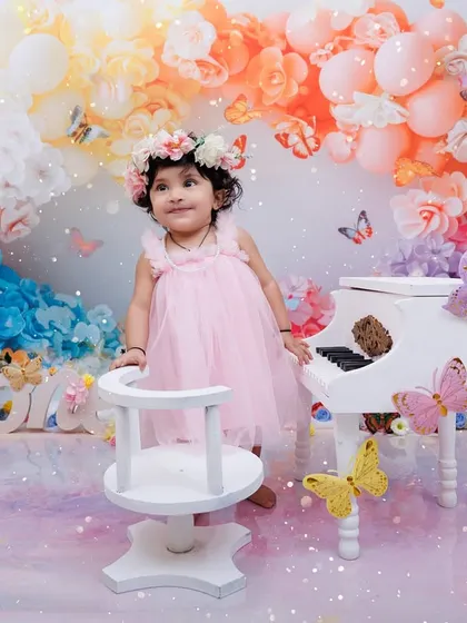 A whimsical first birthday scene with a little girl, a miniature piano, and a colorful backdrop of balloons and flowers.