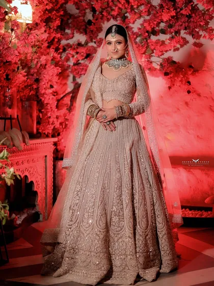 A full-length portrait of the bride against the red floral wall, showcasing the entire elegant ensemble.