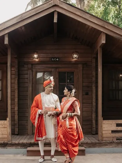 A full-length shot of the couple in their regal Maharashtrian wedding attire, standing before a charming wooden lodge.