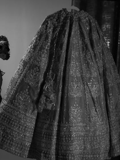 A black and white artistic shot of the bride standing next to her lehenga. It creates a sense of anticipation and drama.