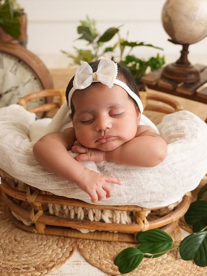 This setup features a sleeping newborn in a basket surrounded by vintage-inspired props like a clock and globe, suggesting the timeless journey of life ahead.