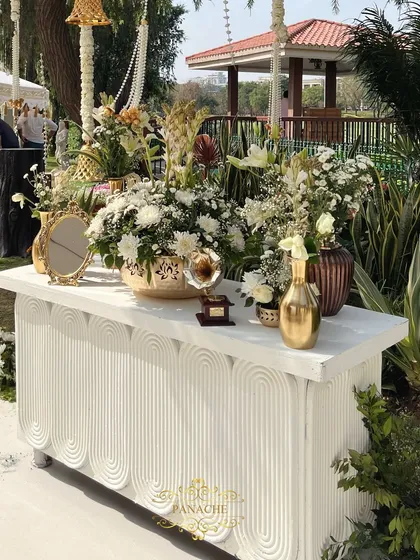 A stylish welcome console table, decorated with an abundance of white flowers, golden vases, and vintage props.