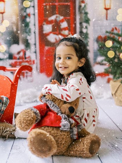 A little girl hugging her teddy bear in a snowy Christmas setup. A sweet and innocent moment.