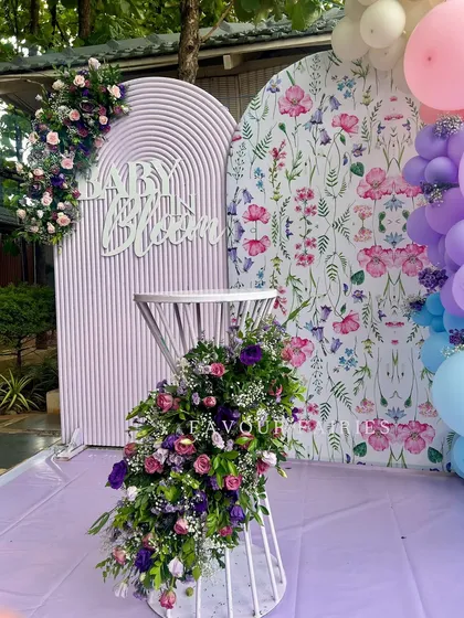 A 'Baby in Bloom' setup with a beautiful mix of textures and patterns. The decor combines a slatted lavender backdrop with a floral print panel, adorned with fresh flower arrangements.