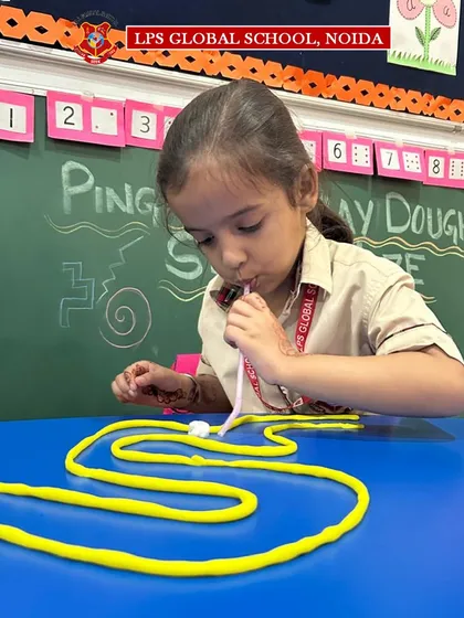 A young learner carefully blows a ping pong ball through a winding straw maze. This activity is one of the many ways we make skill-building an enjoyable and interactive experience.