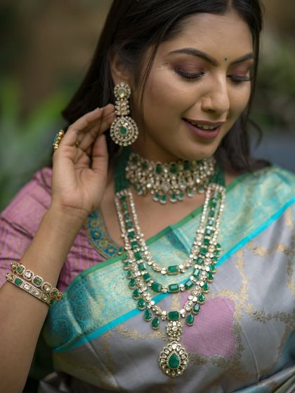 A close-up on the exquisite emerald jewelry that perfectly complements the cool tones of the grey, blue, and lavender saree.