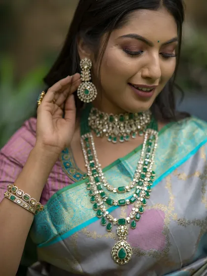 A close-up on the exquisite emerald jewelry that perfectly complements the cool tones of the grey, blue, and lavender saree.