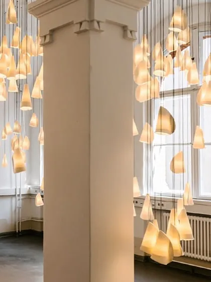 A dense cluster of Bocci 21 pendants wraps around a structural column, turning an architectural necessity into a beautiful feature. The unglazed porcelain has a soft, natural texture.