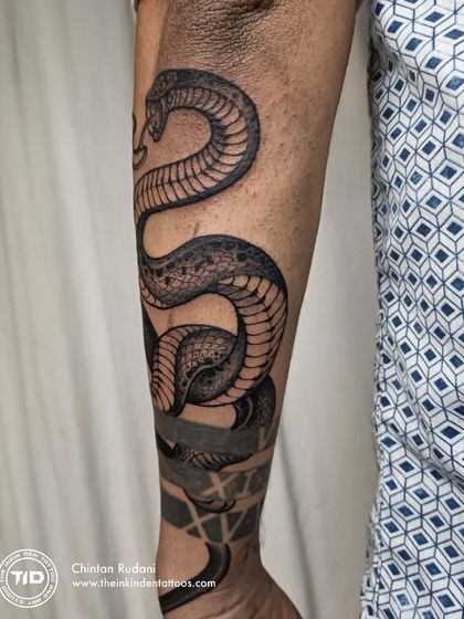 A realistic snake tattoo wrapping around the forearm. The detailed scales and shading, combined with the solid black bands, create a dynamic and powerful design that moves with the arm.