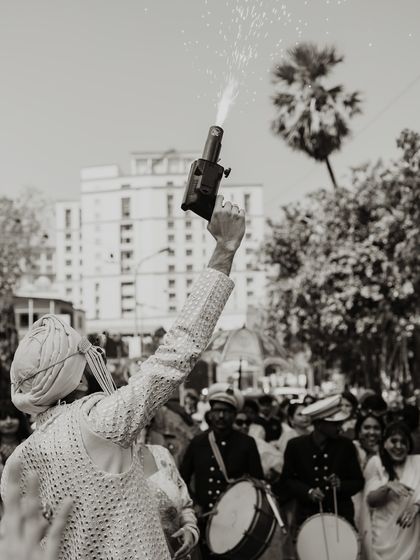 A dynamic black and white shot from the baraat, capturing the celebratory gunfire that adds to the energy of a Punjabi wedding procession.