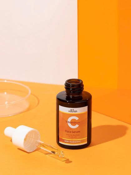 A classic product shot with a focus on the key ingredient. The open serum bottle is paired with petri dishes and a vibrant orange background, giving it a clean, scientific, and energetic feel.