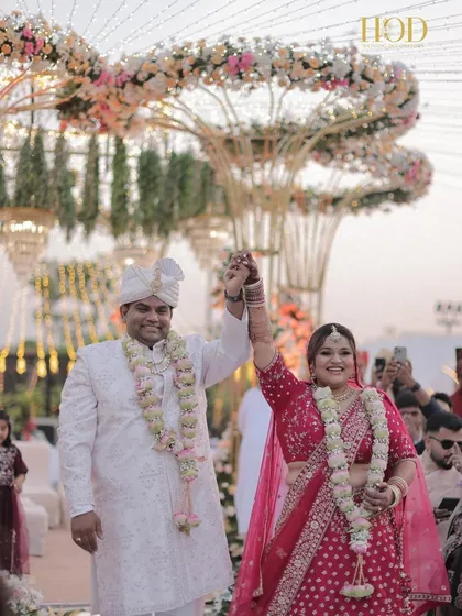 The happy couple after their ceremony, walking down the mirrored aisle with their hands raised in celebration, under the beautiful floral structure.
