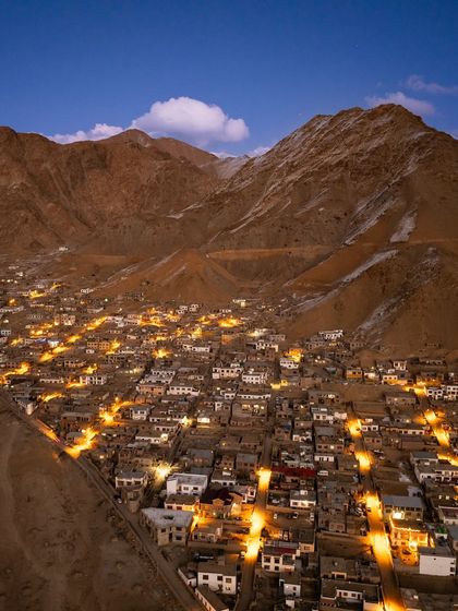 The town of Leh in Ladakh, nestled in a valley and illuminated at dusk. This aerial photograph shows how human settlement coexists with the immense scale of the mountains.
