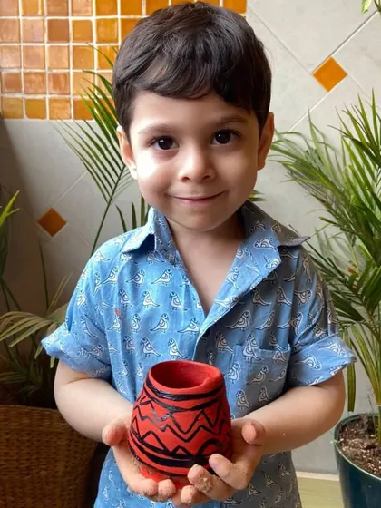Proudly presenting a finished piece. This little boy holds up his hand-painted pot, a tangible result of his focus, creativity, and hard work at our center.