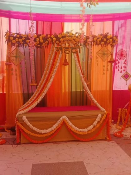 A simple and traditional seating arrangement for a Haldi or Pooja ceremony. The backdrop uses colorful drapes and is decorated with flower garlands.