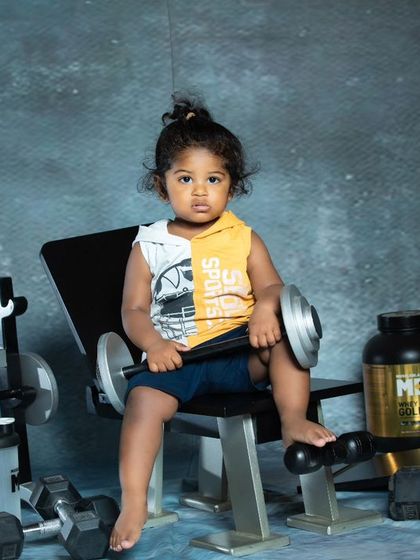 A serious-looking toddler contemplating his next workout, surrounded by weights and a protein shaker.