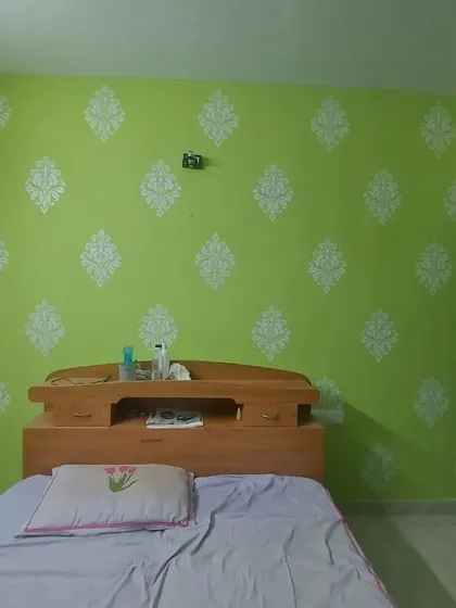 A bedroom accent wall featuring a classic damask stencil pattern in white over a vibrant lime green base. Stenciling is a great way to add an elegant, decorative touch to any room.