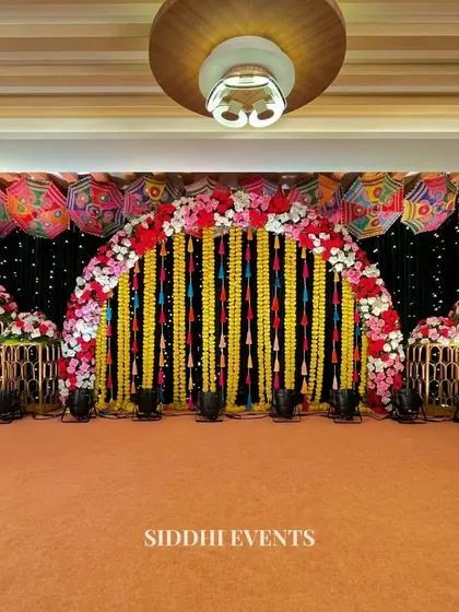 We designed this spectacular stage for a vibrant Haldi ceremony. A canopy of colorful Rajasthani umbrellas and a dramatic black backdrop make the floral arch and hanging marigold garlands pop, creating a truly grand and festive focal point for the event.