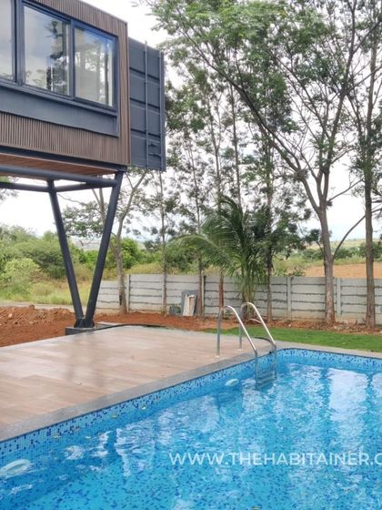 The pool and deck area of a hybrid container home, with the cantilevered bedroom visible above.