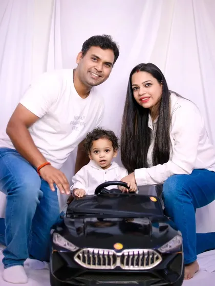 A classic family portrait with a simple white background, featuring parents and their son in his toy car.