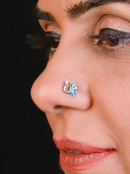 A delicate silver nose pin with a floral design and a touch of blue, adding a subtle pop of color.