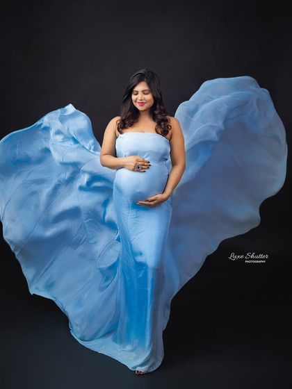 A serene portrait of an expectant mother in a flowing light blue gown, her hands gently cradling her bump.