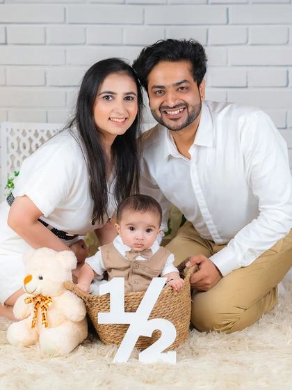 A perfect family shot from a half-birthday session. The baby sits in a basket, framed by his loving parents and a cute teddy bear.