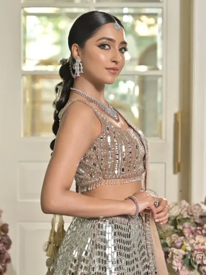 A three-quarter view of the model, where the start of the modern braid is visible. The hairstyle is kept sleek at the crown to balance the heavily detailed lehenga and jewellery.