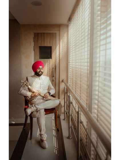 A classic portrait of the groom, Avikash, seated by a window, holding his kirpan. The natural light creates a thoughtful and regal mood.