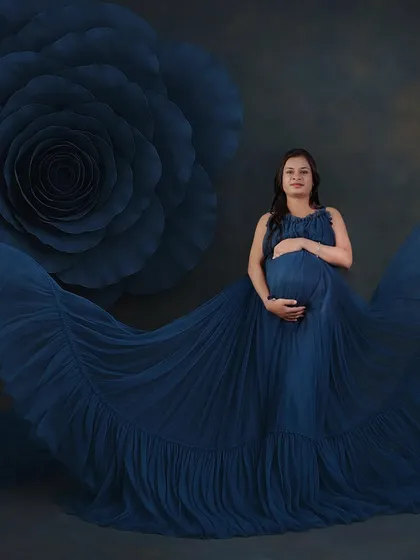 This is a high-fashion inspired maternity portrait. The combination of the bold blue gown and the oversized floral prop creates a stunning, artistic image that makes the mother-to-be the star of the show.