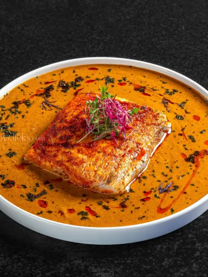 A modern take on a fish curry. The vibrant orange gravy and artistic plating create a fine-dining look.