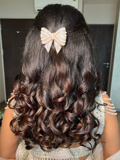A cute pearl bow adds a touch of modern charm to her soft, wavy hairstyle, completing the engagement look.