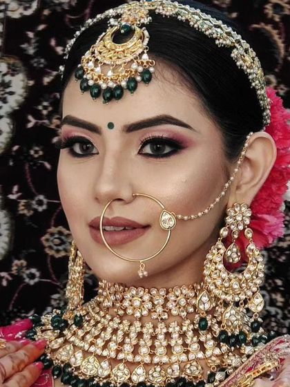 A close-up of a bride wearing a heavy Kundan choker with green beads and a matching pink flower in her hair.