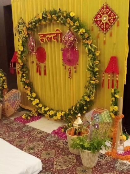 An indoor Haldi setup with a circular marigold backdrop and traditional Rajasthani hangings. The yellow fabric draping and patterned carpet complete the festive look.