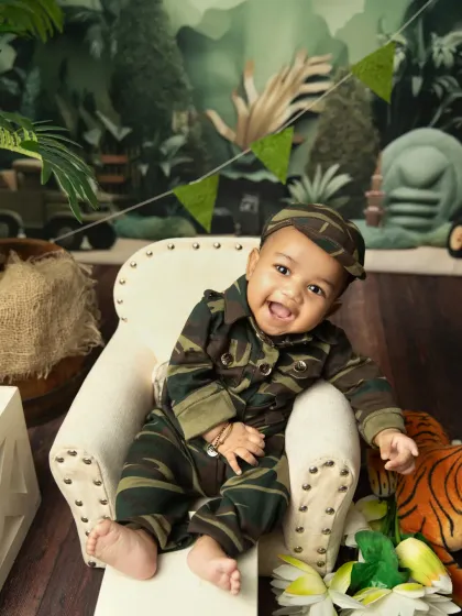 Small smiles, big pride. This little warrior is celebrating a national holiday in a camouflage outfit, complete with a jungle-themed backdrop.