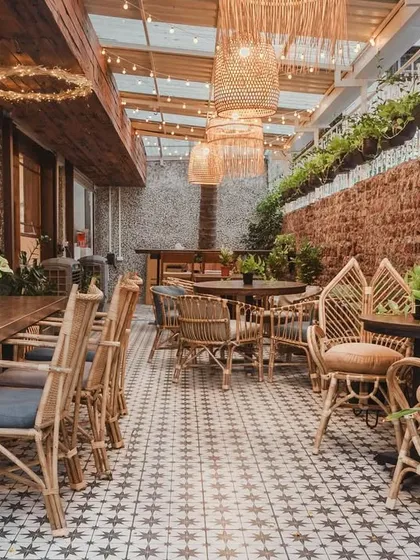 This is a wider view of our serene outdoor cafe area, a versatile space that can be set up for long table brunches or smaller, cozy seating arrangements under our beautiful woven lamps.