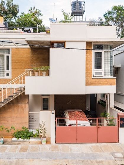 The Vruksha residence, a simple and humble home designed for three sisters in Bangalore. The exterior showcases a mix of mud blocks and painted surfaces, with an external staircase providing access to the upper floor.