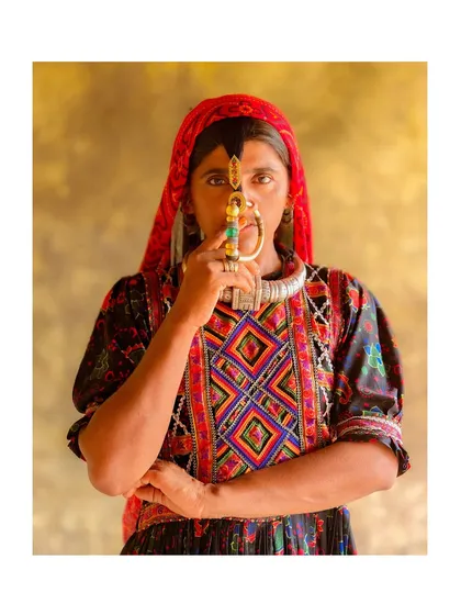 A formal portrait of a Dhaneta Jat woman holding her nose ring. The simple background and direct pose give the image a timeless, archival quality.