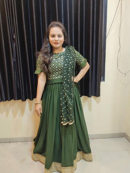 A full-length view of a custom-designed dark green lehenga choli. The combination of the patterned blouse and the simple, flowing skirt with a thick golden border is a classic choice for any festival.