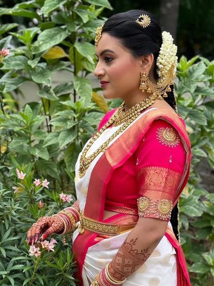 The elegance of a traditional South Indian bride. This shot highlights the beautiful pairing of the antique gold jewellery with the classic white and pink silk saree, a timeless combination.