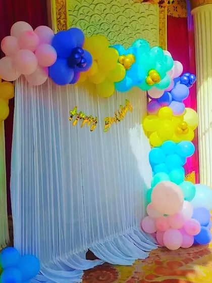 A simple selfie booth for a birthday, with a white curtain backdrop and a colorful balloon arch.