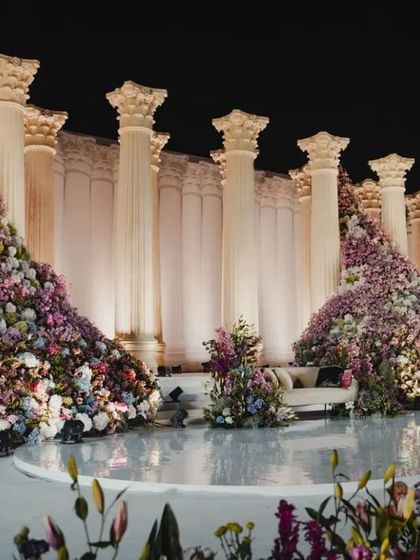 A full view of the Roman pillar stage, showcasing the balance between the sleek, man-made pillars and the wild, organic abundance of the flowers.
