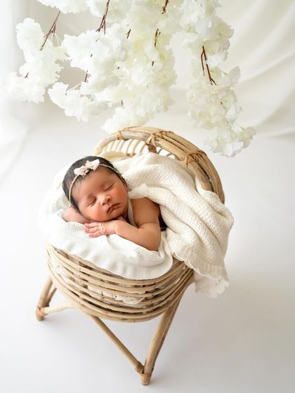 A wider shot of the same baby in a beautiful rattan bassinet, with delicate white flowers hanging overhead. This creates such a serene and dreamy scene.