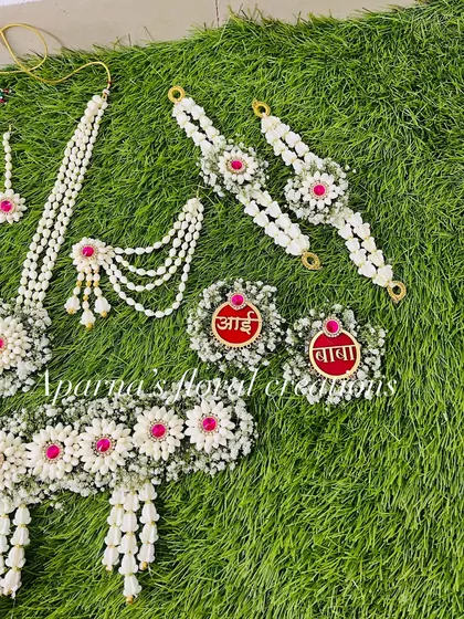 A partial view of a baby shower jewellery set, showing the kamarband, haath phool, and the 'Aai' and 'Baba' brooches in red and white.