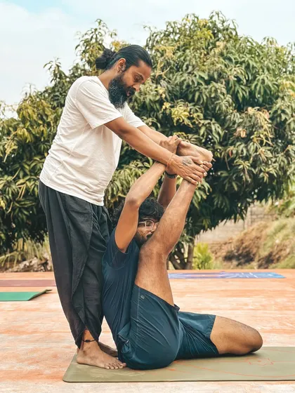 I assist a student in Supta Virasana (Reclining Hero Pose) with a leg extension, a deep stretch for the quadriceps and psoas that requires careful guidance to be performed safely.